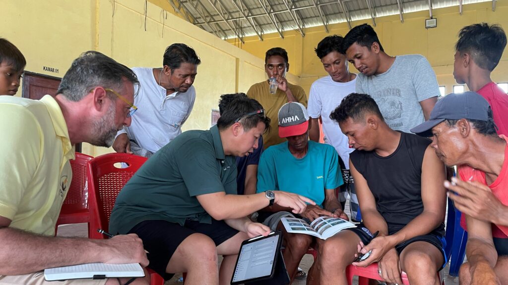 Campaign Director Paul Anderson (left) and Rare's Applied Science Director Raymond Jakub (center left) consult with Indonesian fishers to ID aquarium fish species found on their local reefs.